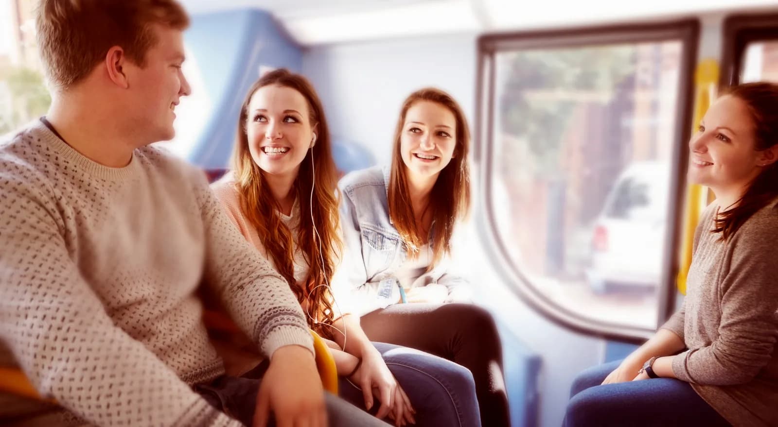 Four young adults are smiling and laughing while riding on a bus.